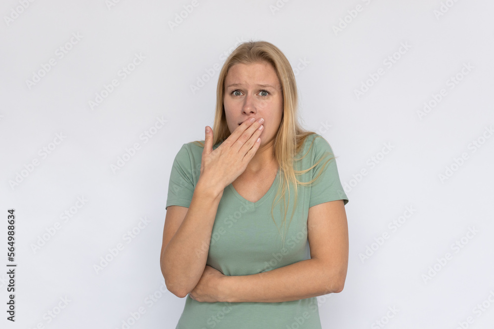 Shocked young woman covering mouth. Portrait of happy Caucasian female model with fair hair in green T-shirt looking at camera with wide eyes, receiving news. Shock, gossip concept Shocked young woman covering mouth. Portrait of happy Caucasian female model with fair hair in green T-shirt looking at camera with wide eyes, receiving news. Shock, gossip concept