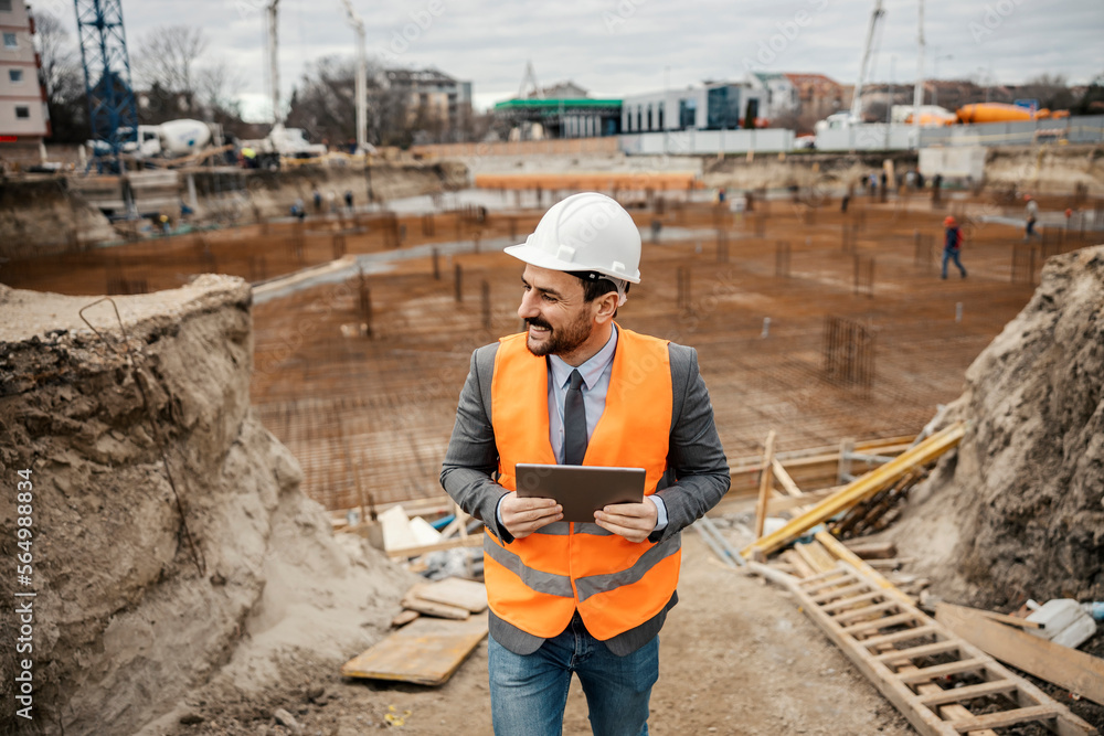 Fototapeta premium A happy contractor is visiting construction site and checking on tablet if everything is fine.
