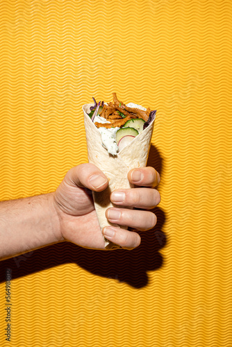 Close-up of a fastfood pita gyros sandwich held by a male hand, yellow background