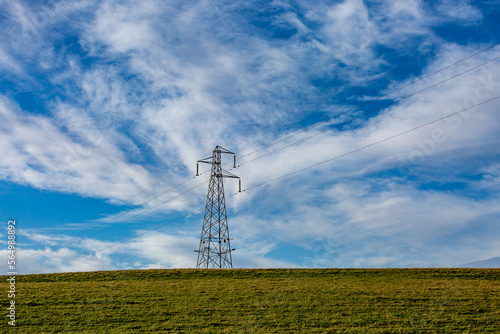 An electricity pylon in the Sussex countryside with blue sky and wispy clouds overhead