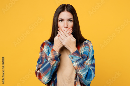 Young sad scared frightened astonished caucasian woman wears blue shirt beige t-shirt cover mouth with hand look camera isolated on plain yellow background studio portrait. People lifestyle concept.