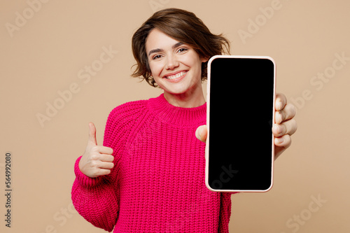 Foto Young happy fun woman wear pink sweater hold use close up mobile cell phone with blank screen workspace area show thumb up isolated on plain pastel beige background studio