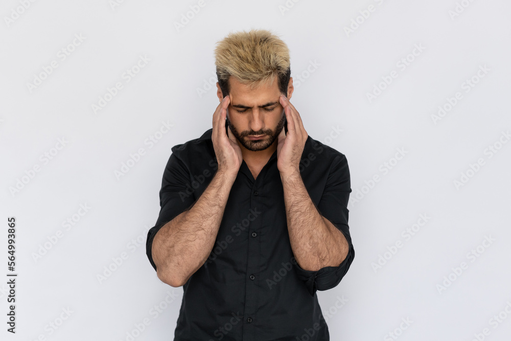 Portrait of stressed young man rubbing head on white background. Caucasian guy with stubble and highlighted hair wearing black T-shirt suffering from headache. Migraine or stress concept Portrait of stressed young man rubbing head on white background. Caucasian guy with stubble and highlighted hair wearing black T-shirt suffering from headache. Migraine or stress concept