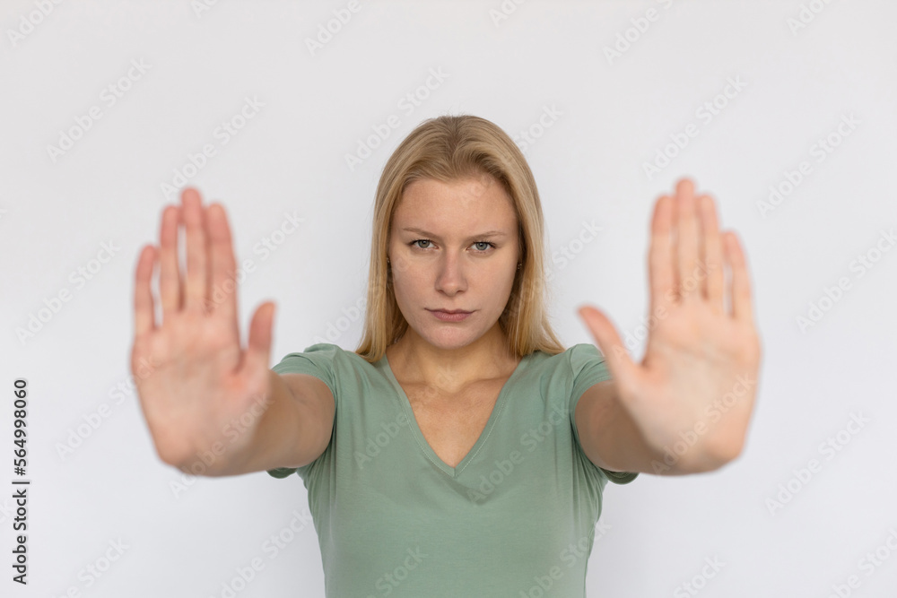 Angry young woman showing stop sign. Strict Caucasian female model with fair hair in green T-shirt looking at camera with open palms, protesting against something. Refusal, warning concept Angry young woman showing stop sign. Strict Caucasian female model with fair hair in green T-shirt looking at camera with open palms, protesting against something. Refusal, warning concept