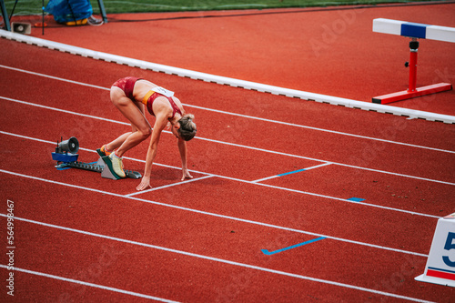 Female athlete at the starting line of a 400m race on track, captured in a dynamic and powerful pose. Suitable for sports and fitness campaigns, highlighting determination and focus