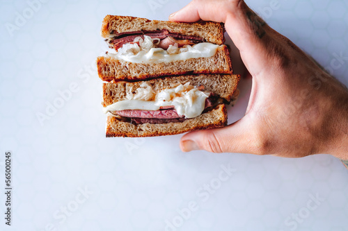 Male Person holding reuben sandwich with white background. Corned beef, pastrami, cheese and sauerkraut. Classic New York dish photo