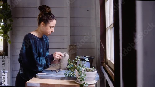 Potter puts the finishing touches on clay vase in her workship photo
