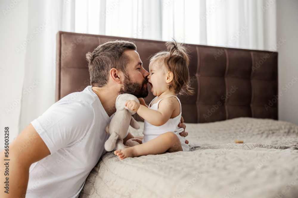 A father is rubbing noses with his little girl while she is sitting on a bed and speaking something. A father is rubbing noses with his little girl while she is sitting on a bed and speaking something.
