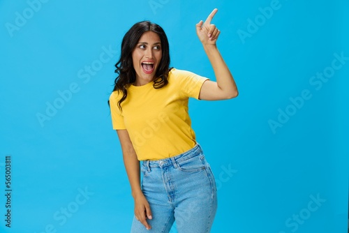 Woman in yellow t-shirt on blue background posing gestures emotions and signals with smile, hands up happiness copy space