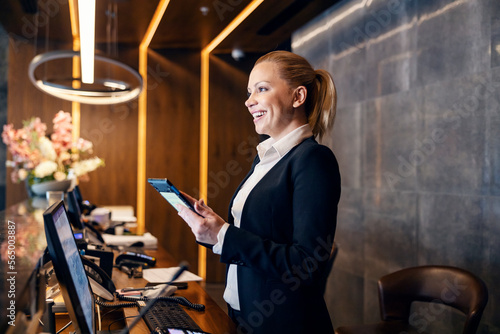 Vászonkép A happy receptionist is talking with hotel guest and making a reservation on a tablet