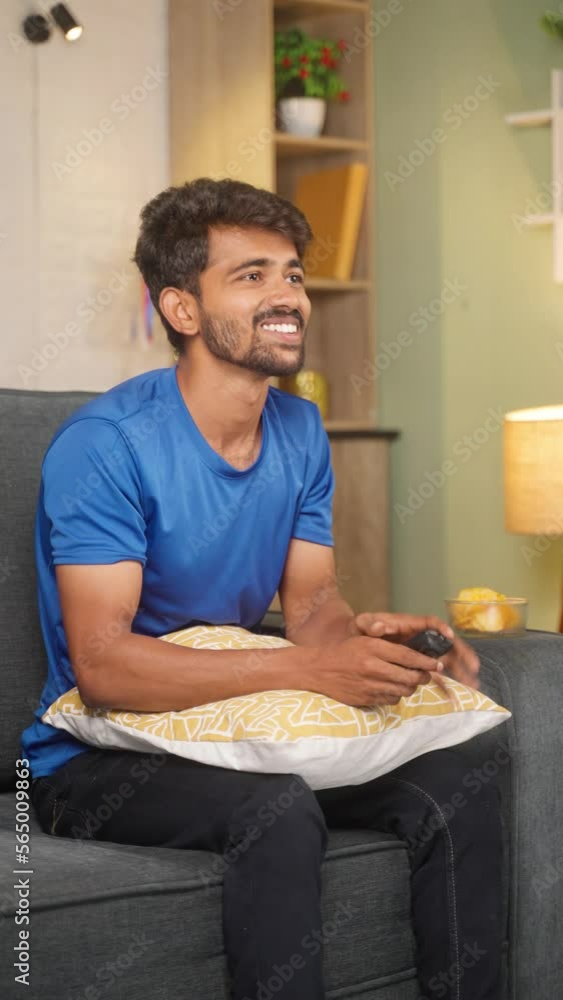 Vertical shot of smiling young man using mobile phone while sitting on sofa at home - concept of social media sharing, internet and smart phone addiction. Vertical shot of smiling young man using mobile phone while sitting on sofa at home - concept of social media sharing, internet and smart phone addiction.