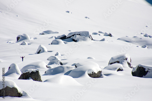 French skiing guide crosses over a pristine snowfield. Arm outstretched, untouched powder and large boulders.