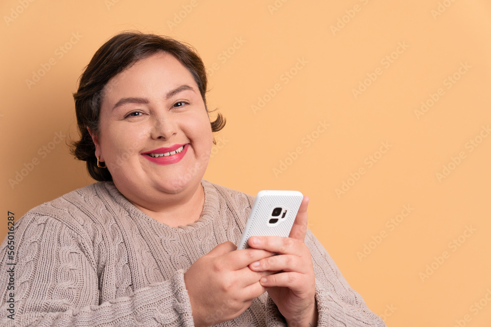 joyful plus size woman texting and typing on the mobile smartphone in beige background. communication, app, connection concept. joyful plus size woman texting and typing on the mobile smartphone in beige background. communication, app, connection concept.