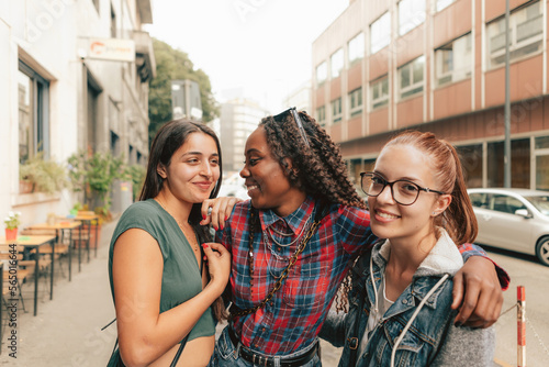 Wallpaper Mural three female friends of different ethnicities hugging and smiling together on the sidewalk of a city street Torontodigital.ca