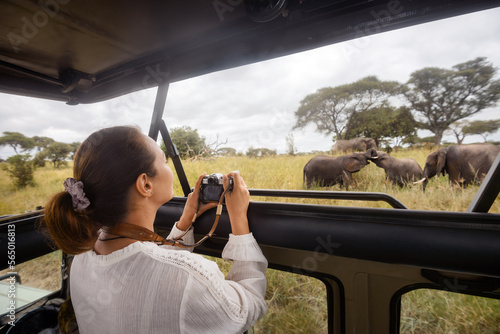 Happy woman on an African safari travels by car with an open roof and photograph wild elephants