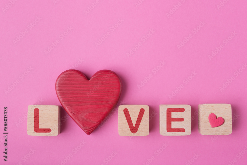 Word Love made of wooden blocks and decorative valentines heart. Pink background with copy space. Valentine’s day conceptual greeting