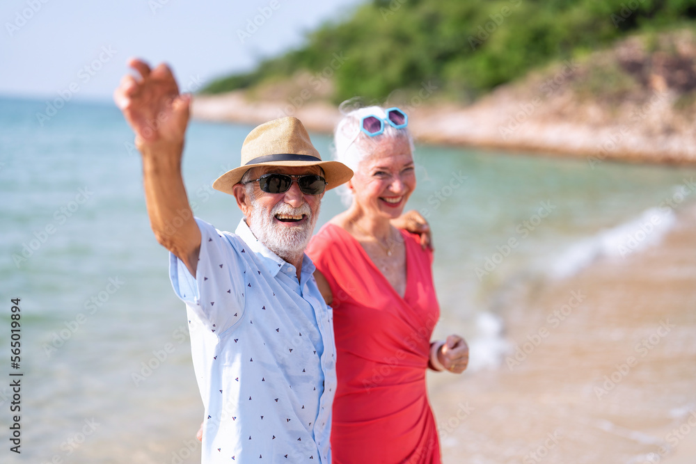 Couple of old mature people walk together on the sand at the beach enjoying and living the moment