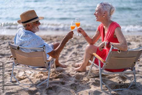 Couple old mature people on the sand at the beach sitting enjoying drink juice and living the moment