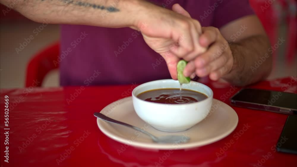 Slow motion of a latin man squeezing a lime into his broth stock soup in a mexican restaurant on a red table Slow motion of a latin man squeezing a lime into his broth stock soup in a mexican restaurant on a red table