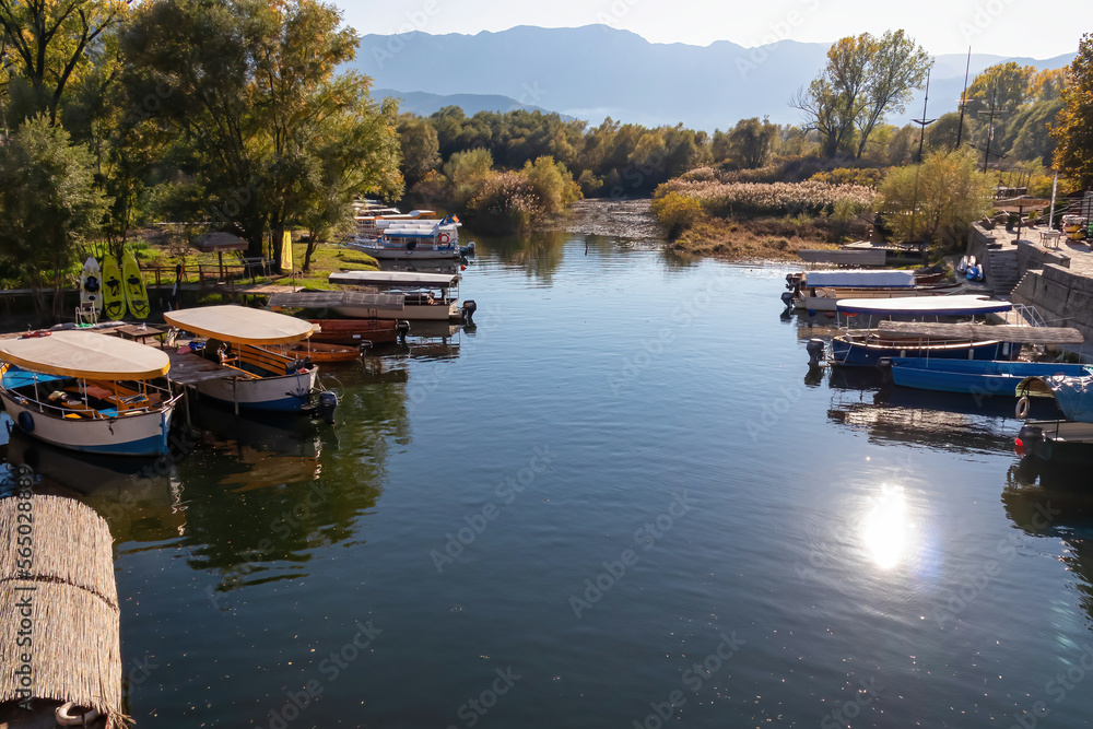 Panoramic idyllic view of small colorful boats floating on Crmnica river going to Lake Skadar in Virpazar, Bar, Montenegro, Balkans, Europe. Travel destination in the Dinaric Alps. Vrsuta peak