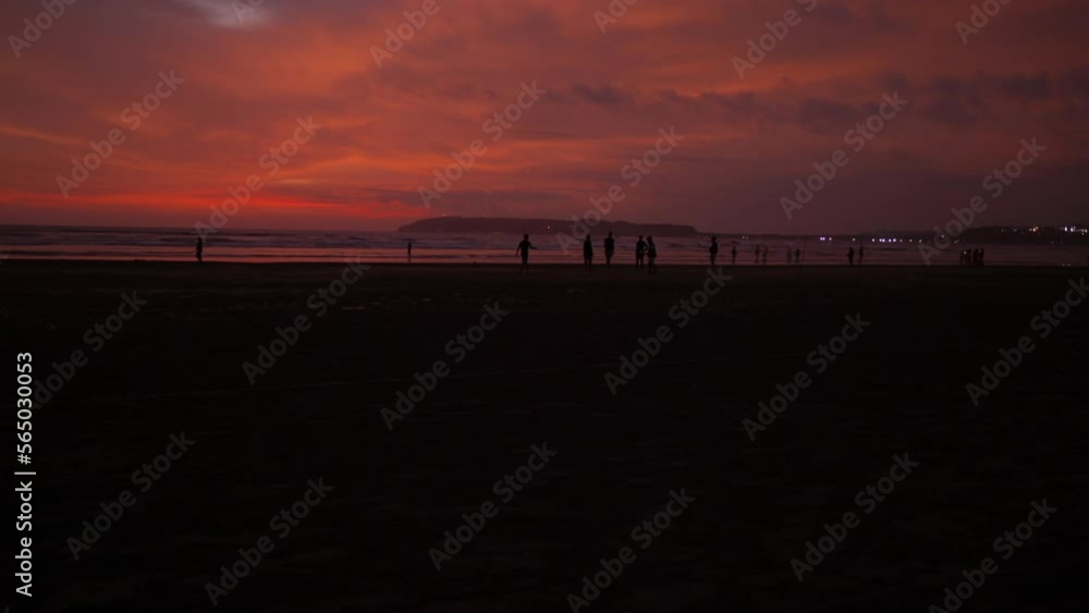 Seascape view of people silhouettes on a sandy coastline, during a bright red sunset, on a cloudy evening Seascape view of people silhouettes on a sandy coastline, during a bright red sunset, on a cloudy evening