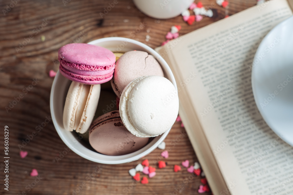 Macaroons in a bowl, a cup of coffee, on a background of small hearts on a wooden background Macaroons in a bowl, a cup of coffee, on a background of small hearts on a wooden background