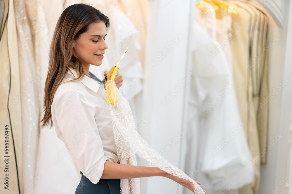 Caucasian young is smiling while choosing wedding dress in modern wedding salon Caucasian young is smiling while choosing wedding dress in modern wedding salon
