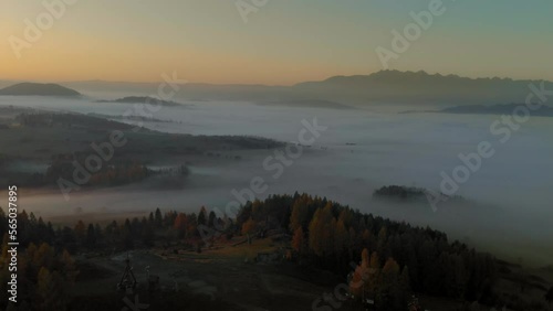 Aerial shot olish ountryside with hills and fields covered in morning mist with yellow sunrise and orange sky. Trees in the foreground. photo