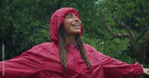 Portrait of Joyful Woman in a Red Raincoat Smiling and Laughing as the Rain Falls on her Face. Happy and Carefree Female Adult Surrounded by Greenery Connecting with her Inner Child  photo