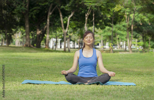 young attractive asian woman sitting on the matt and doing yoga in the park among nature atmosphere © Verin