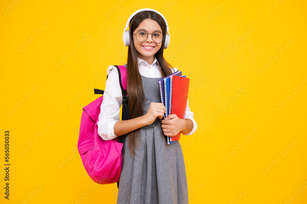 Schoolgirl, teenage student girl in headphones hold books on yellow isolated studio background. School and music education concept. Back to school. Happy face, positive and smiling emotions