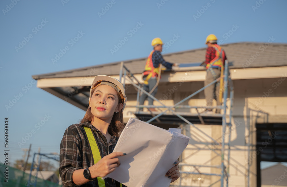 Portrait of a young beautiful engineer woman working in a construction building. Close-up of a female engineer at the construction site with man worker installing solar panels on the roof Portrait of a young beautiful engineer woman working in a construction building. Close-up of a female engineer at the construction site with man worker installing solar panels on the roof