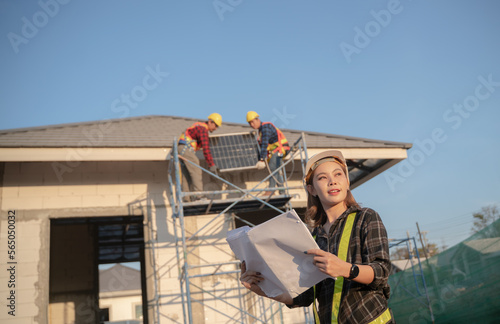 Portrait of a young beautiful engineer woman working in a construction building. Close-up of a female engineer at the construction site with man worker installing solar panels on the roof