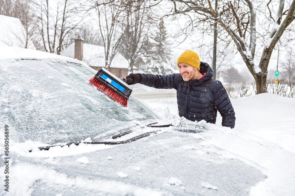 young man cleans his car after a snowfall on a sunny, frosty day