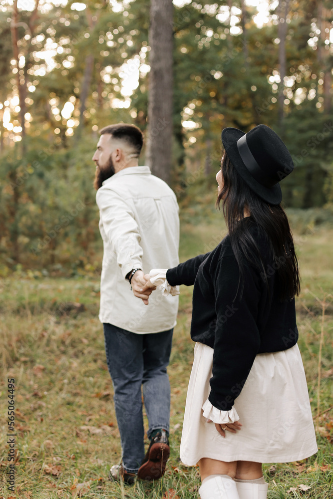 Happy young bearded man with his girlfriend holding hands and walking in the park. Loving stylish couple having fun on date in nature outdoors on warm day. Valentines day. Happy young bearded man with his girlfriend holding hands and walking in the park. Loving stylish couple having fun on date in nature outdoors on warm day. Valentines day.