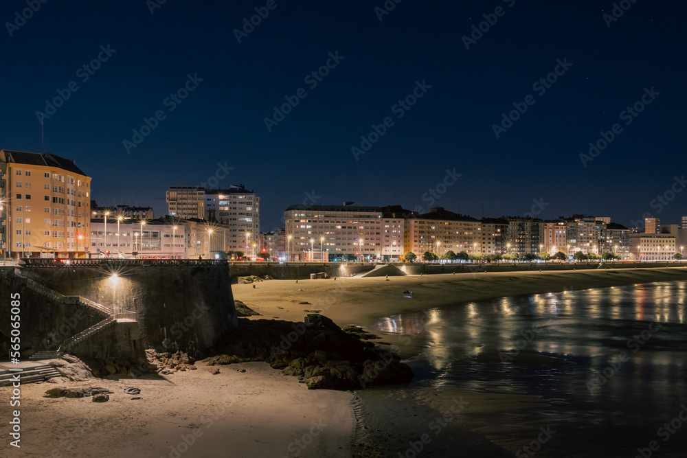 Sandy large beach in the city of A Coruna at night. The lights of the city are reflected in the water.