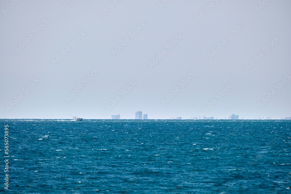 Sea panorama. Small motor boat floats in deap blue bay water under bright blue sky, tall buildings on distant shore Sea panorama. Small motor boat floats in deap blue bay water under bright blue sky, tall buildings on distant shore