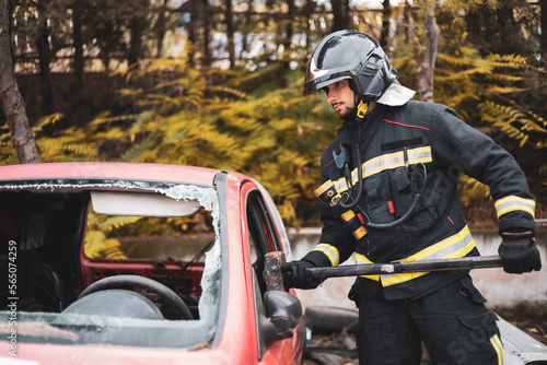 A young and uniformed firefighter breaking the glass of a car that has suffered an accident with a sledgehammer to rescue passengers.