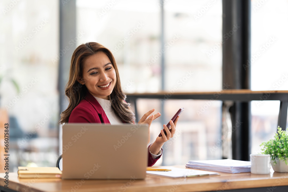 Smiling beautiful Asian businesswoman analyzing chart and graph showing changes on the market and holding smartphone at office. Smiling beautiful Asian businesswoman analyzing chart and graph showing changes on the market and holding smartphone at office.