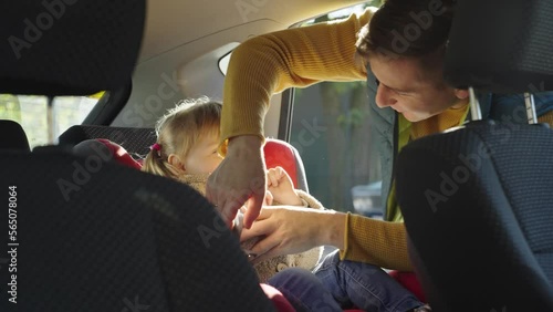 A father puts a child in a car seat. Sunny day. A man fastens a seat belt in a car seat. A little girl gets into a car with her father. High quality 4k footage