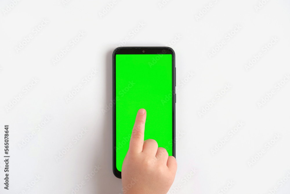 Child hand touching clicking on mobile phone with chromakey screen. Little Baby Finger Taps in the center of blank phone green display. Close up 4K Footage. Using smartphone device. Top view Flat lay Child hand touching clicking on mobile phone with chromakey screen. Little Baby Finger Taps in the center of blank phone green display. Close up 4K Footage. Using smartphone device. Top view Flat lay
