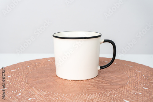 A white blank enamel mug on the top of a rounded mat decorated with the white background