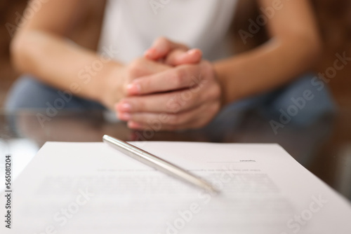 Woman sitting at table with agreement and pen, shallow depth of field.