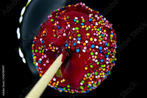 apple on a stick in red caramel with multi-colored icing on a black background