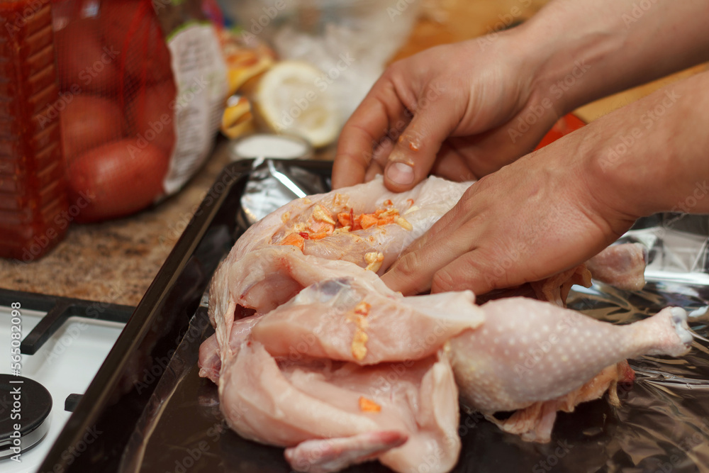 Cook prepares chicken for baking with spices and vegetables in oven in kitchen