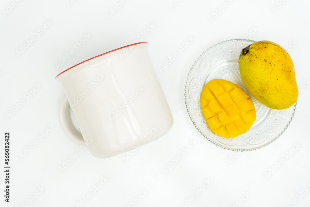 A white blank enamel mug laying out on a white table with a fresh mango close it it A white blank enamel mug laying out on a white table with a fresh mango close it it