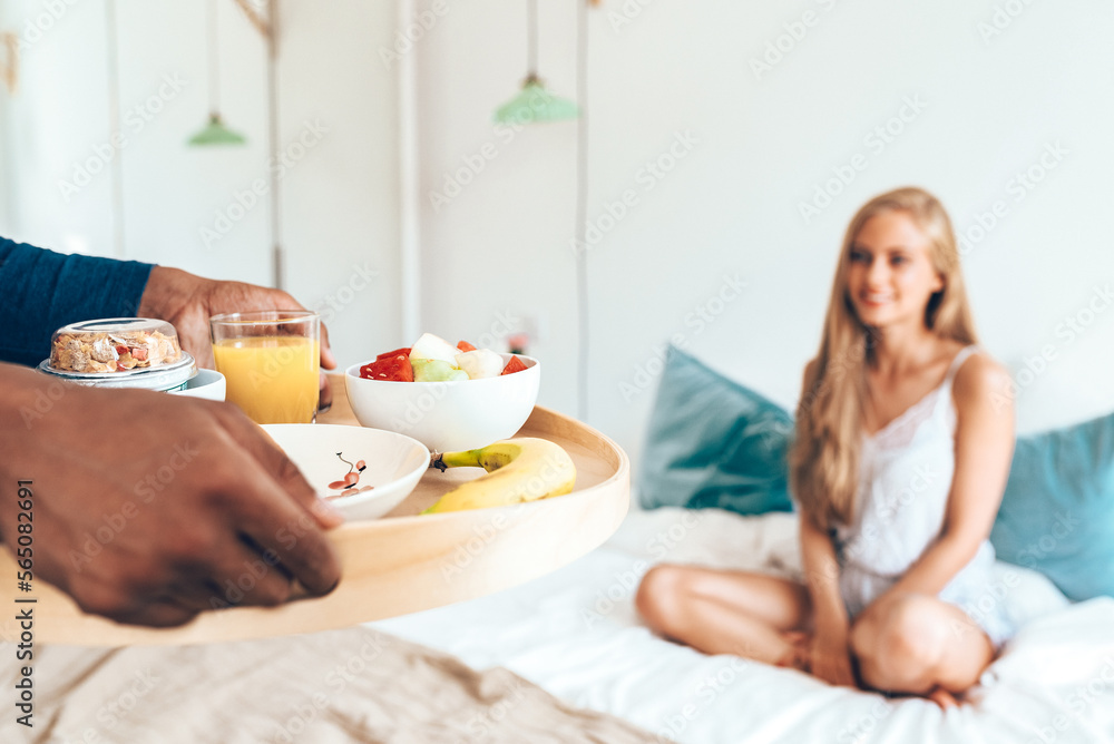 Young beautiful interracial couple having a surprise breakfast in bed .
