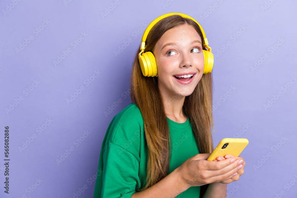 Photo of cheerful adorable lady use hold iphone earbuds gadget look interested empty space offer isolated on purple color background - obrazy, fototapety, plakaty 