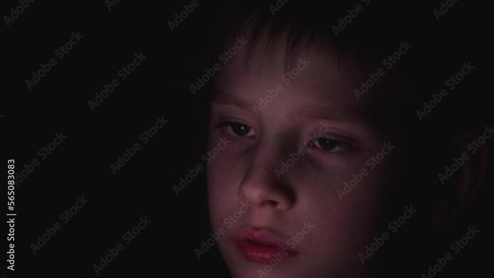 enthusiastic caucasian boy 8 years old looks into a smartphone before going to bed in a dark room. The face of a child illuminated by the light of a smartphone screen . child using social media enthusiastic caucasian boy 8 years old looks into a smartphone before going to bed in a dark room. The face of a child illuminated by the light of a smartphone screen . child using social media