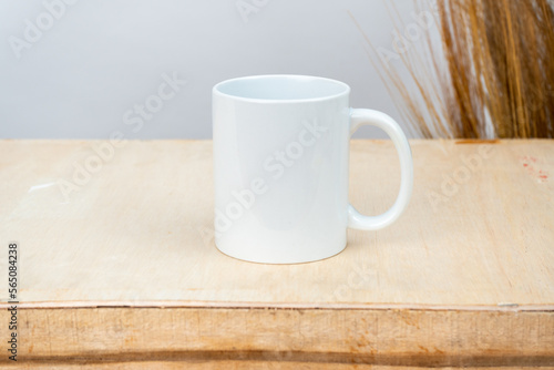 A white blank coffee mug on the top of a plywood with some simple rustic flower at the background